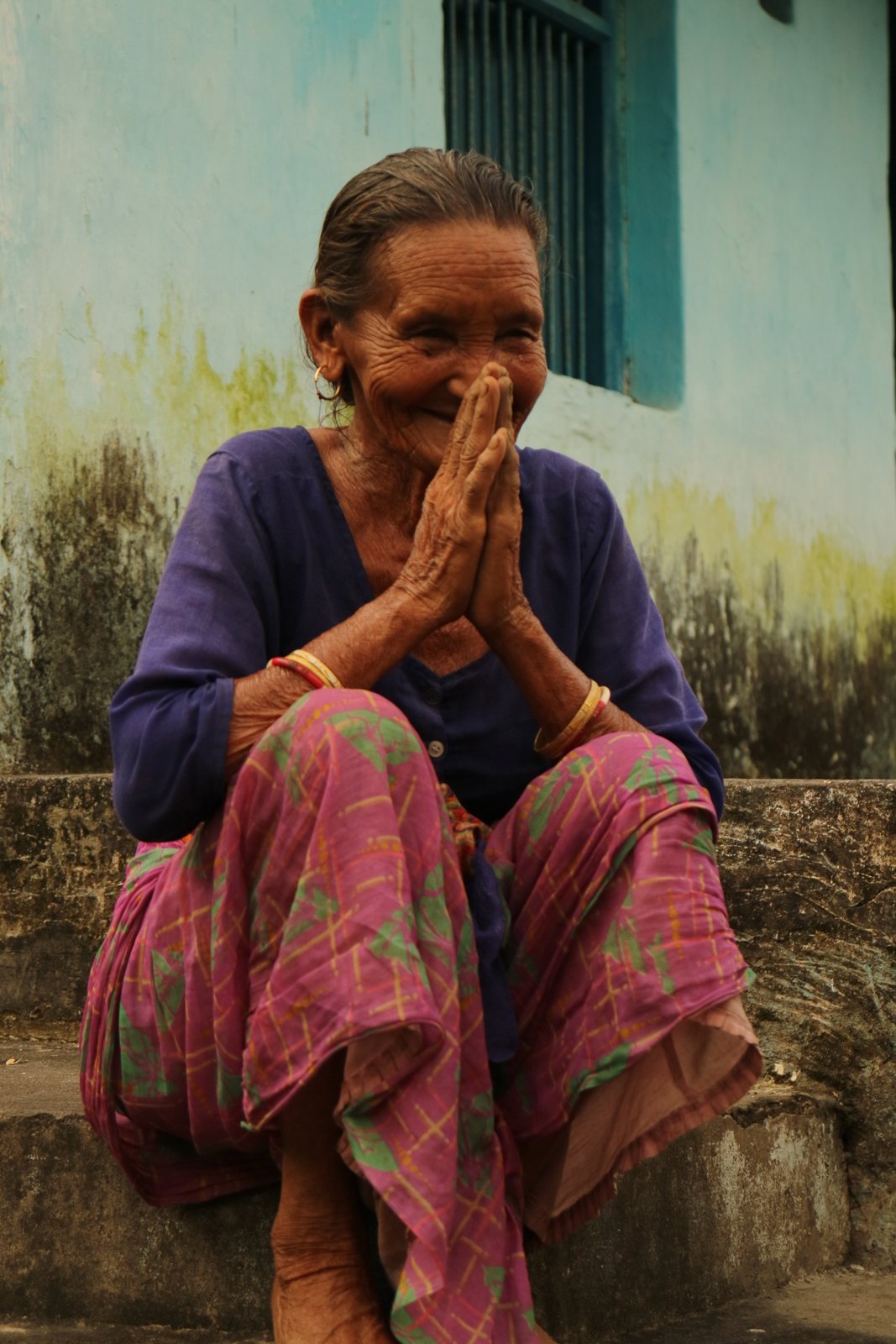 An elderly woman smiling with her hands in namaste